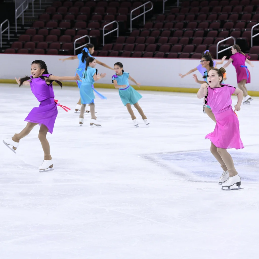 Happy figure skating girls playfully performing fun figure skating activities on ice in colorful dresses