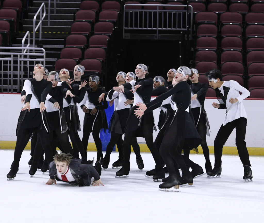 Figure skaters with piano keys as face paint in piano costumes throwing a skater dressed as Beethoven onto the ice
