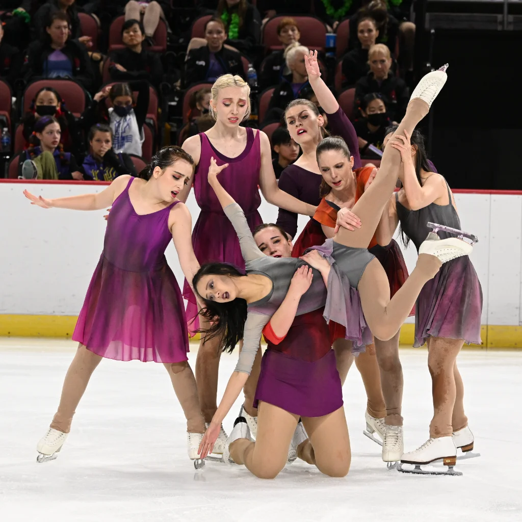 Six figure skaters holding another skater parallel to the ice with a skate in the air
