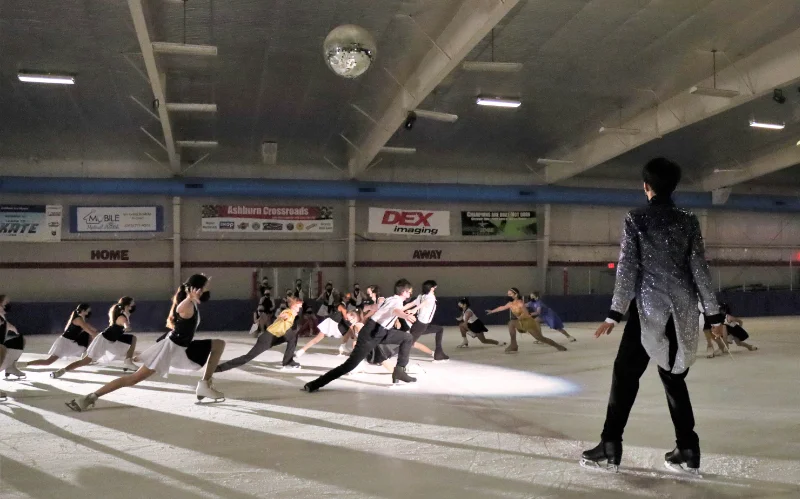 Single skater watching a team perform lunges on ice